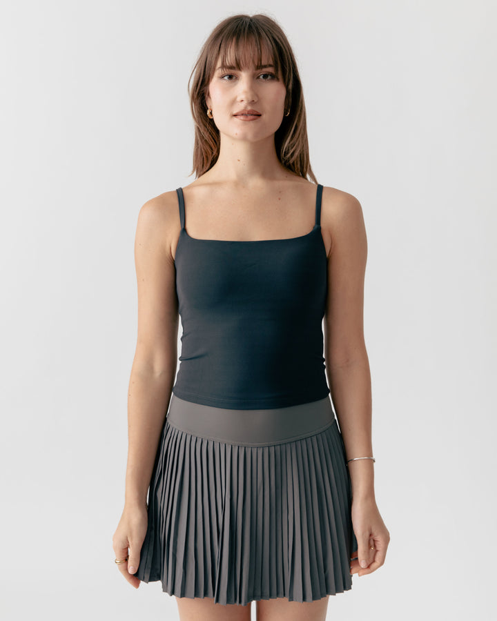 Woman wearing a black tank top and gray pleated skirt on a white background