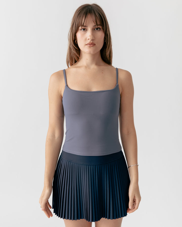 Woman wearing a charcoal camisole square neck tank top and navy pleated skirt