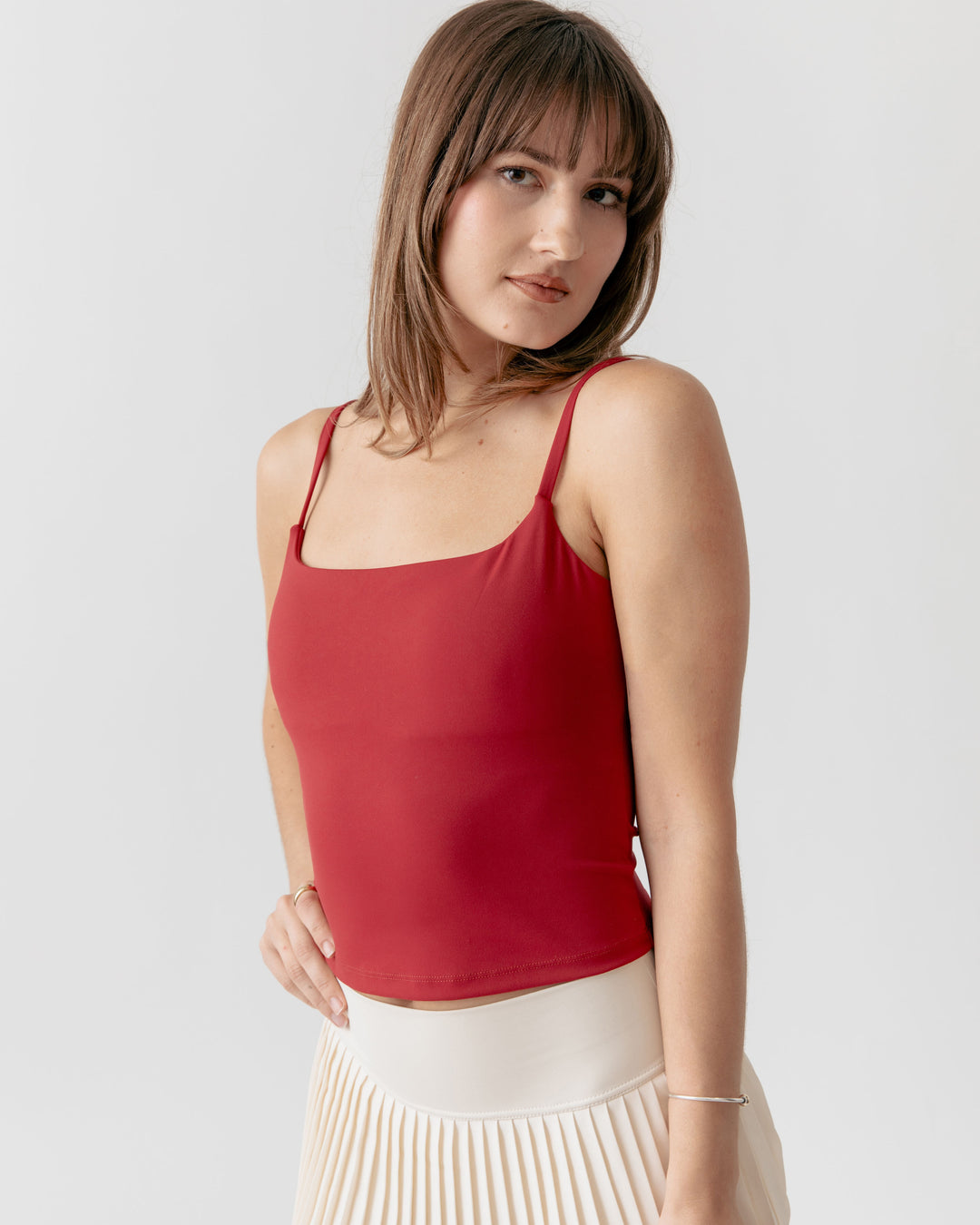 Woman wearing a red camisole tank top and white skirt against a plain background