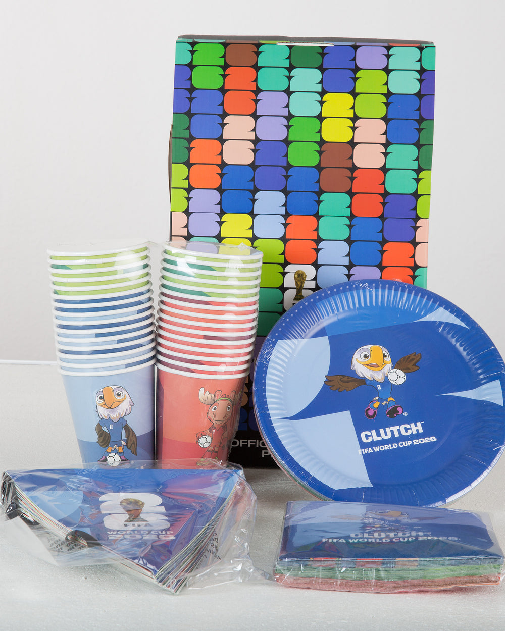 Party supplies including cups, plates, and napkins with a colorful patterned box in the background.