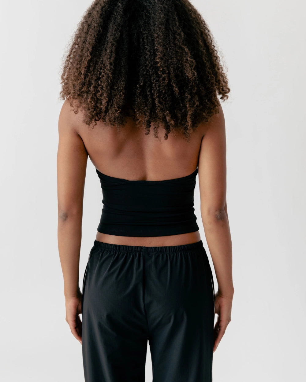 Person wearing a black tube top and black pants on a white background