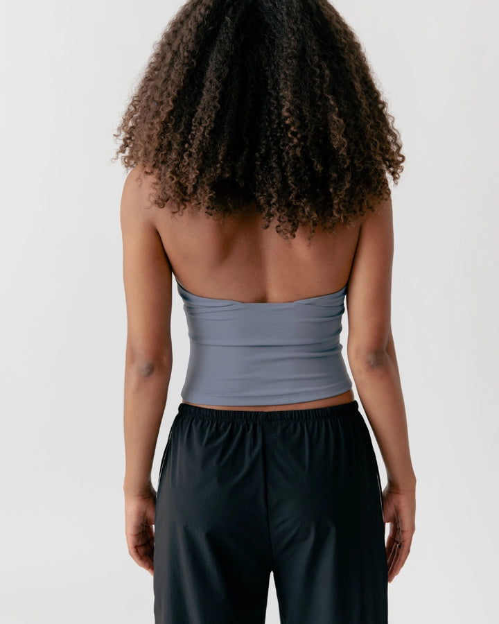Person wearing a light gray strapless top and black pants on a white background