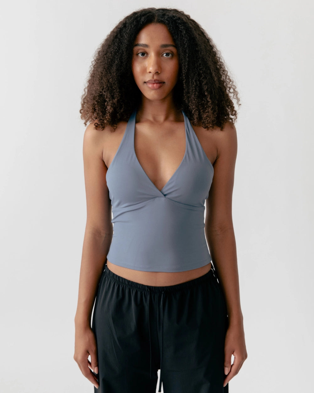 Woman wearing a light blue halter top and black pants on a white background