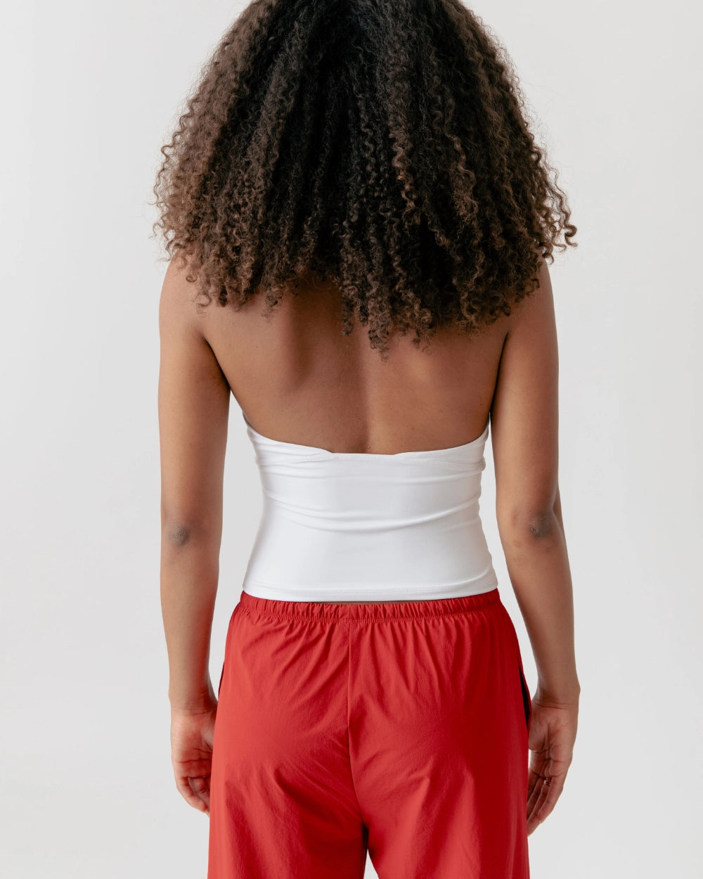 Person wearing a white strapless top and red pants on a plain background