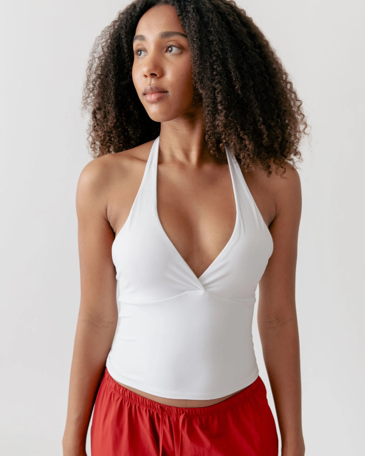 Woman wearing a white halter top and red pants on a plain background