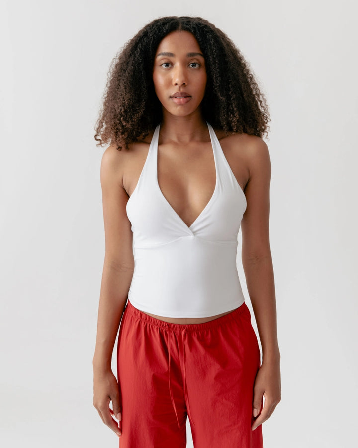 Woman wearing a white halter top and red pants on a light gray background