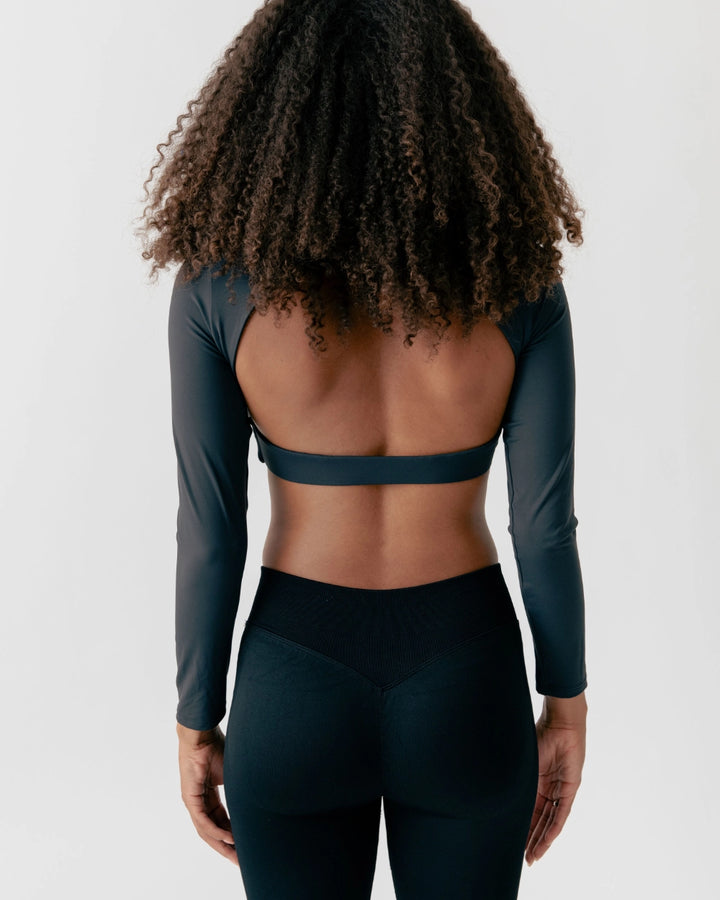 Person wearing a dark green long-sleeve top and leggings on a light gray background