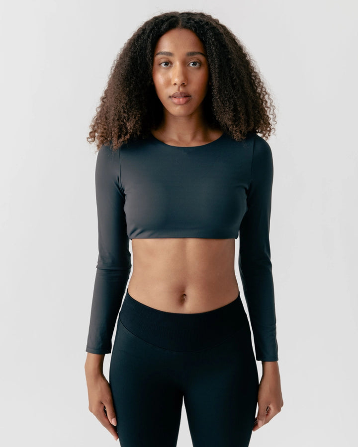 Woman wearing a dark green long-sleeve athletic top and leggings on a light gray background