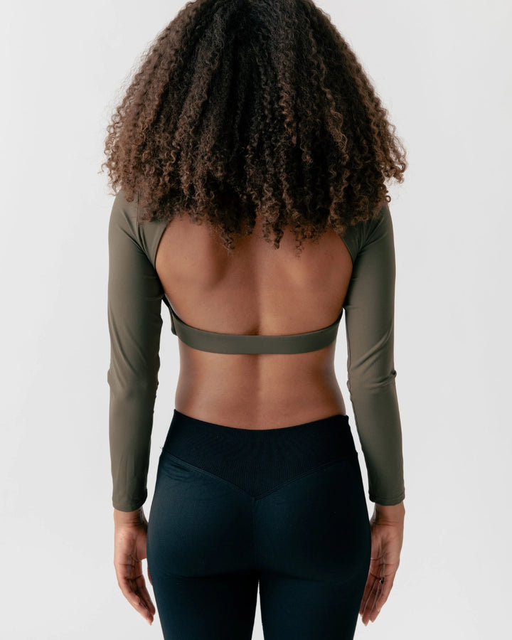 Person wearing a green long-sleeve top and black leggings on a white background