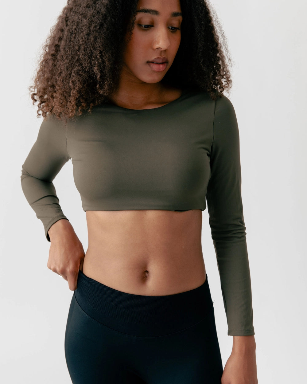 Woman wearing an olive green long-sleeve crop top and black leggings on a white background