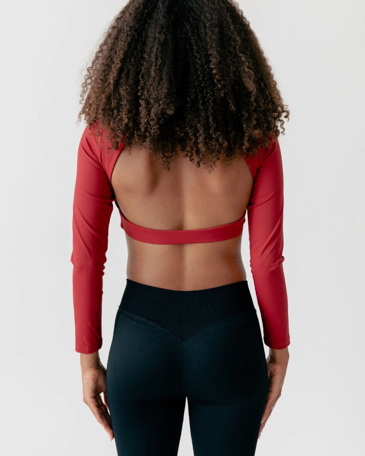 Person wearing a red long-sleeve top and black leggings on a plain background