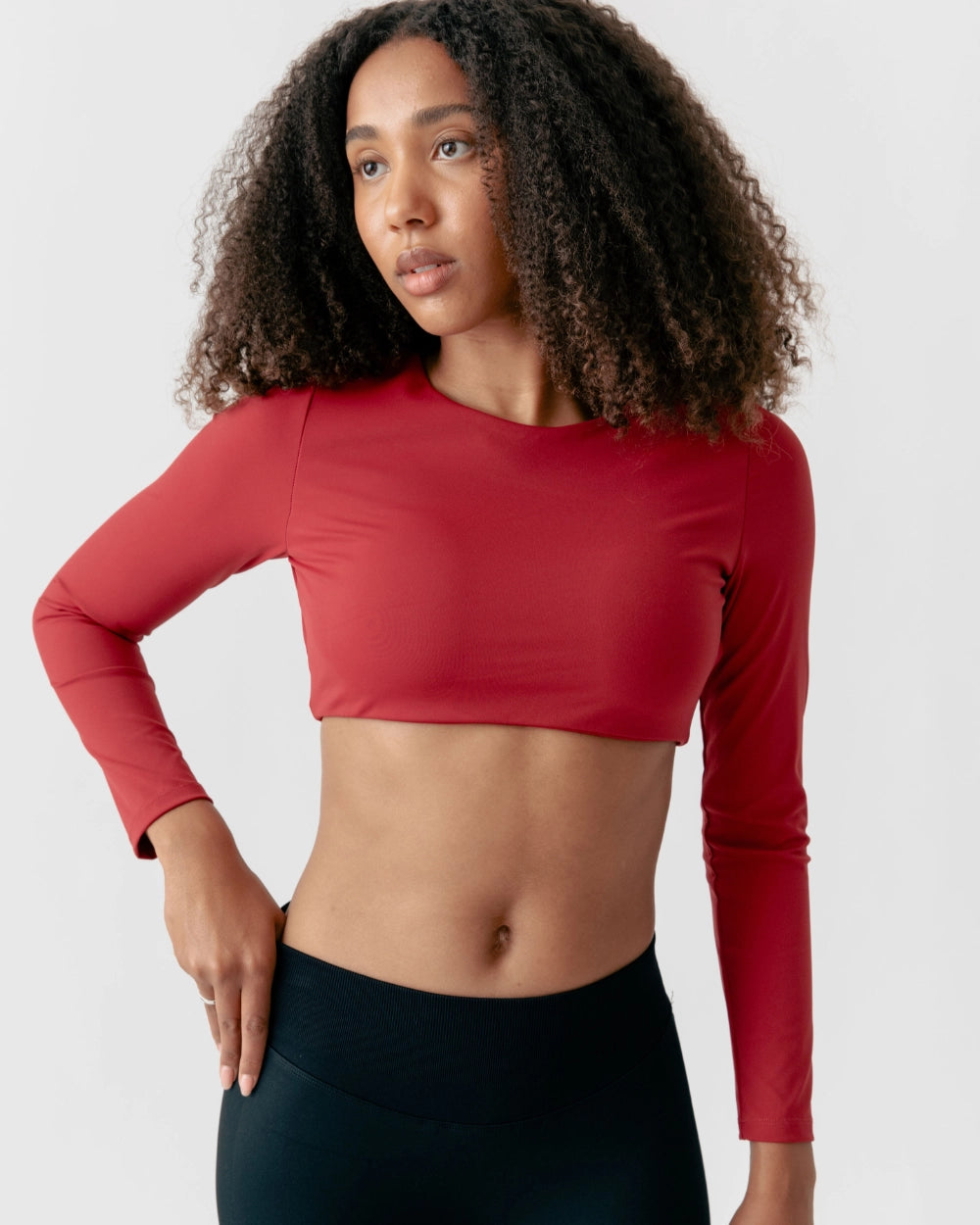Woman wearing a red long-sleeve crop top and black leggings on a light gray background