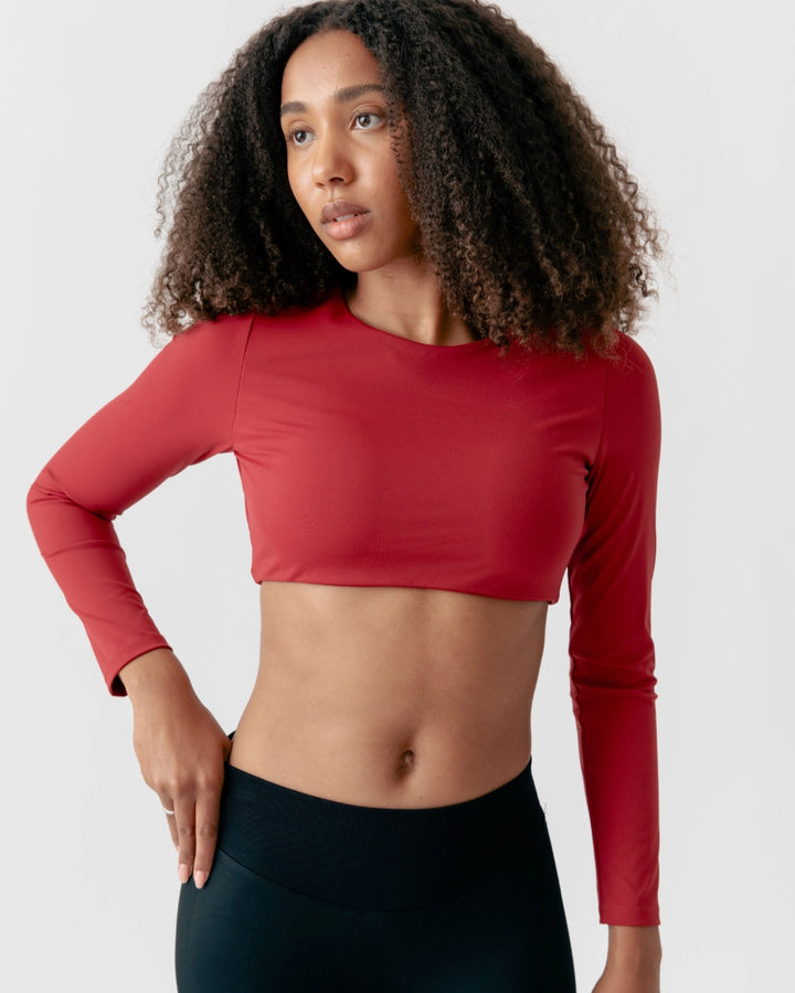 Woman wearing a red long-sleeve crop top and black leggings on a light gray background