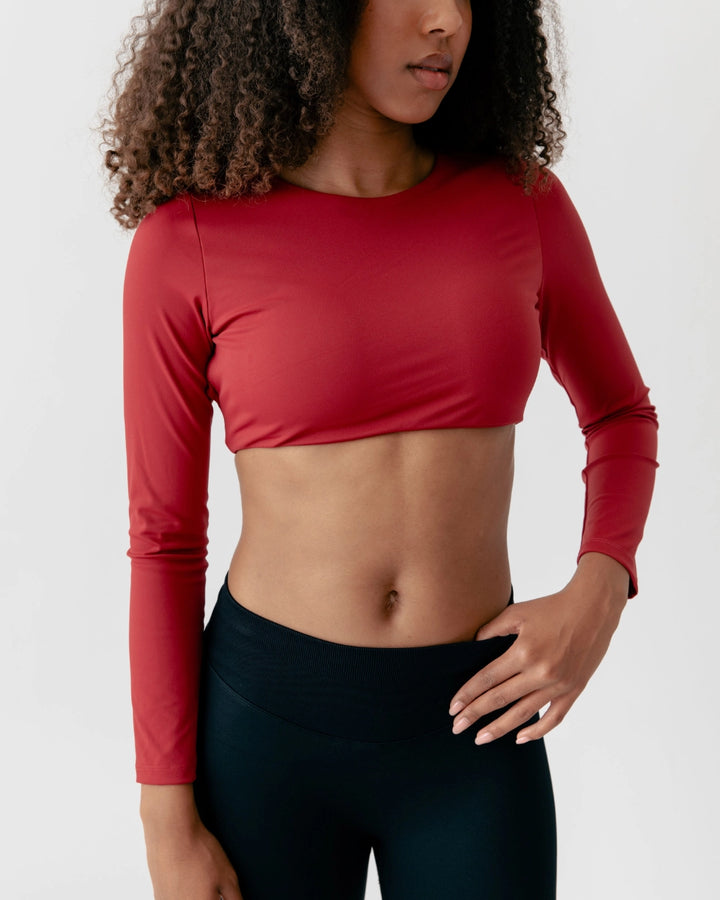 Person wearing a red long-sleeve crop top and black leggings on a white background