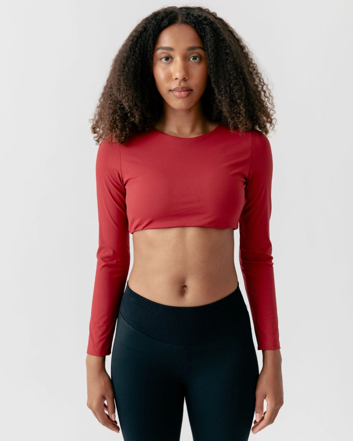 Woman wearing a red long-sleeve crop top and black leggings on a white background