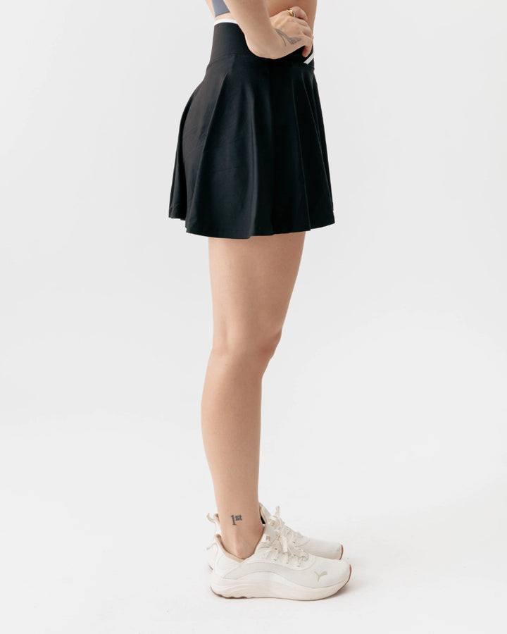 Person wearing a black skirt and white sneakers on a light gray background