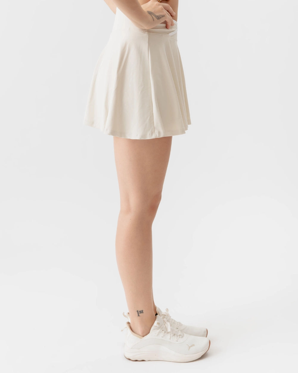 Person wearing a white skirt and white sneakers on a plain background