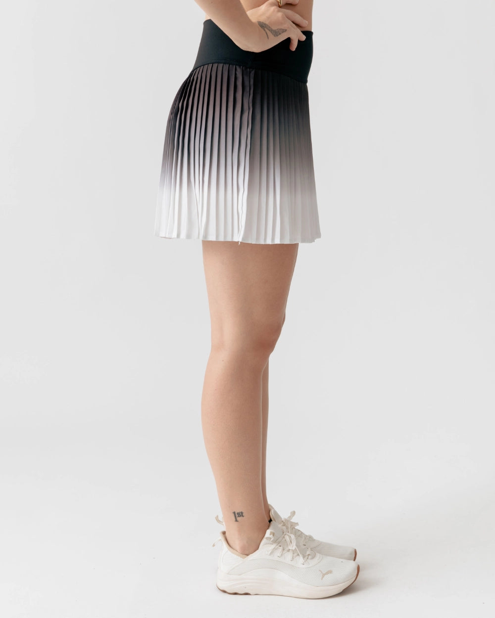 Person wearing a gradient pleated skirt with white sneakers on a light gray background