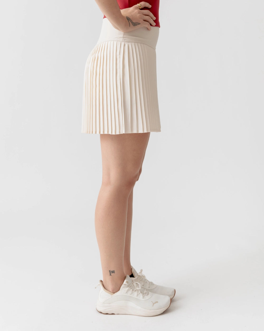 Person wearing a beige pleated skirt and white sneakers on a plain background