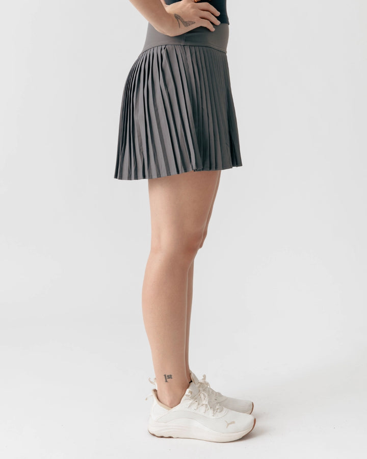 Person wearing a gray pleated skirt and white sneakers on a light gray background