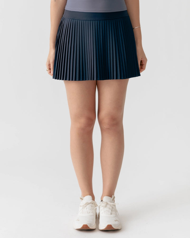 Person wearing a navy pleated skirt on a white background