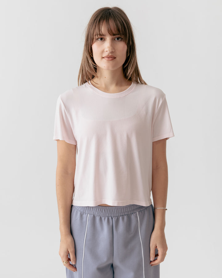 Woman wearing a rose cropped crewneck t-shirt and gray pants on a white background