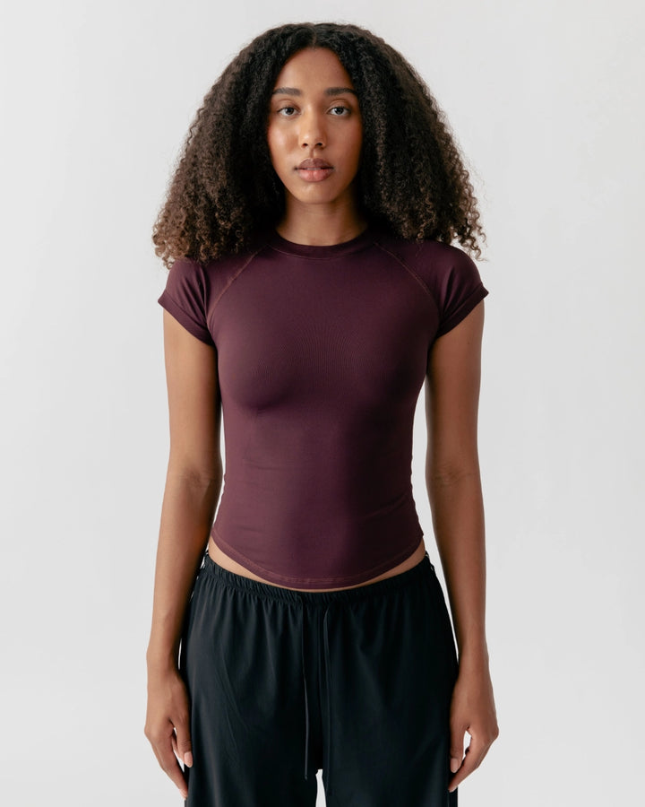 Woman wearing a maroon athletic top and black leggings on a white background