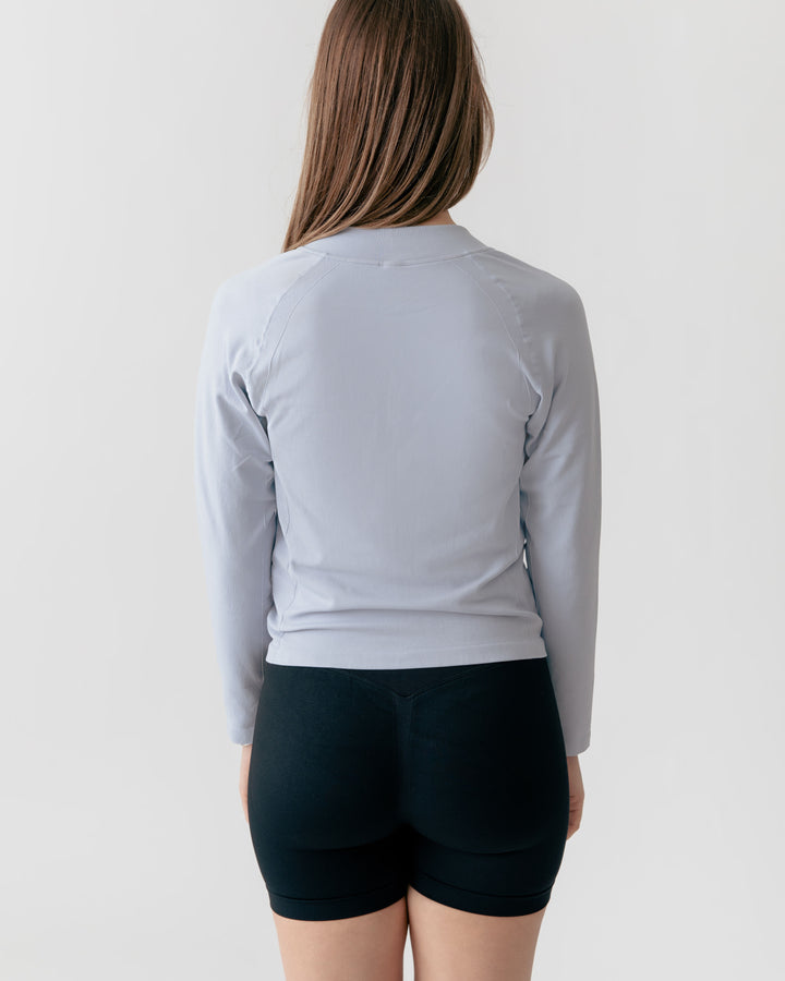 Person wearing a light gray long-sleeve top and black shorts on a plain background