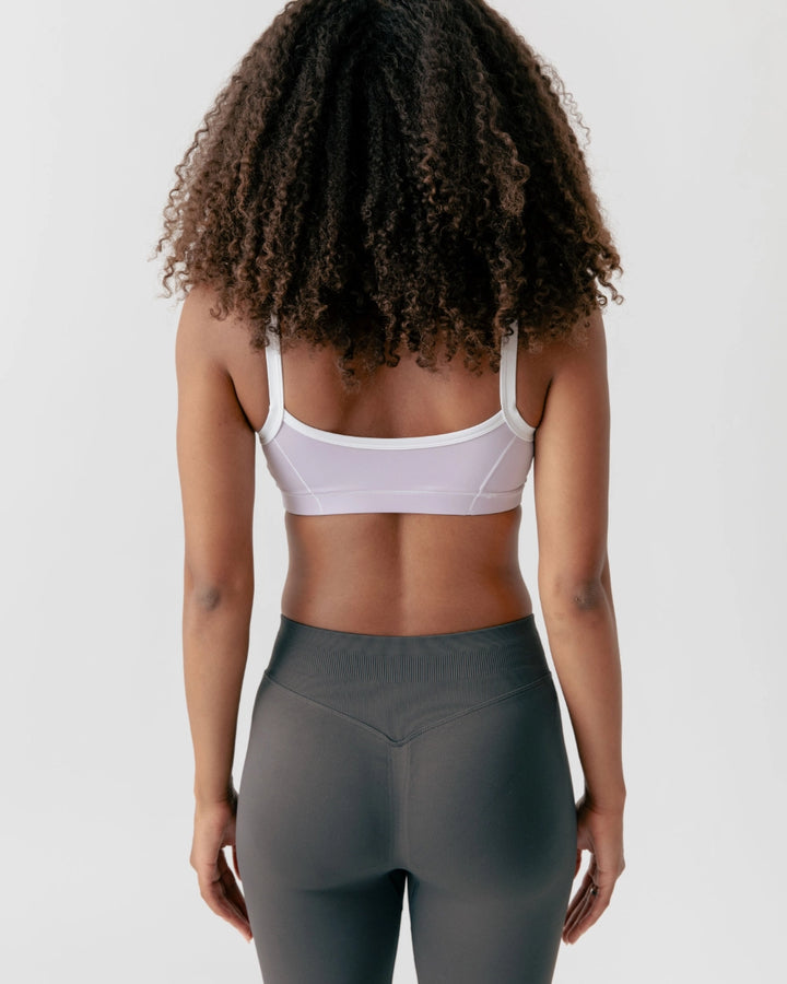Person wearing a white sports bra and gray leggings on a plain background