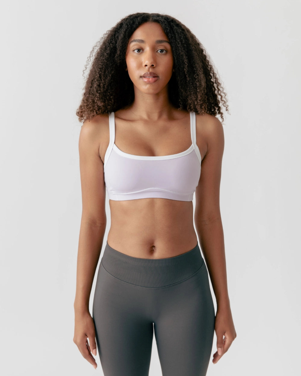 Woman wearing a white sports bra and gray leggings on a light gray background