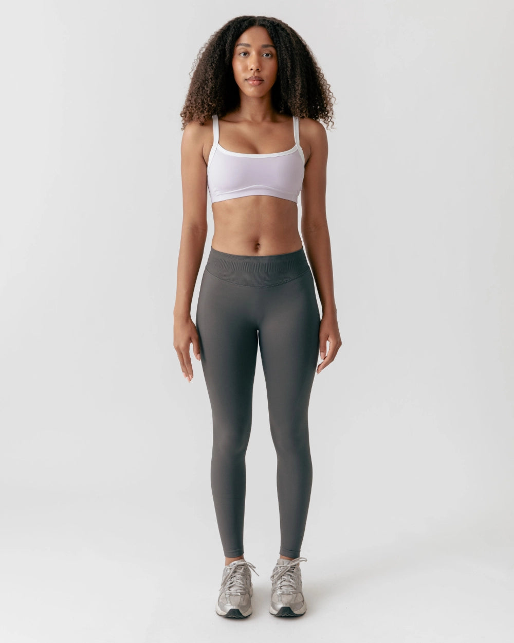 Woman wearing a white sports bra and gray leggings on a white background