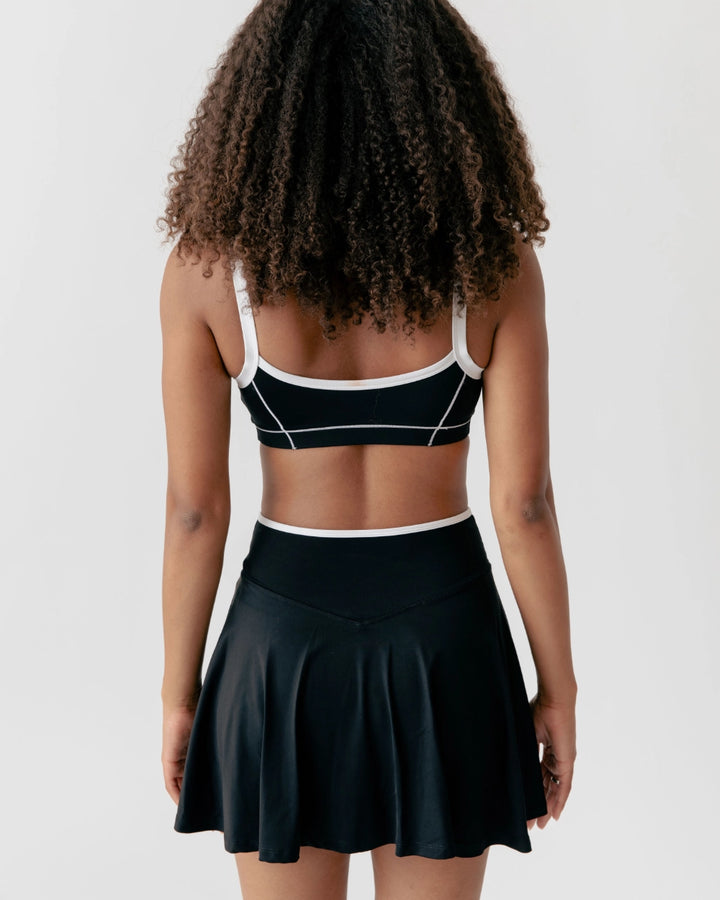 Person wearing a black sports bra and skirt set on a plain background
