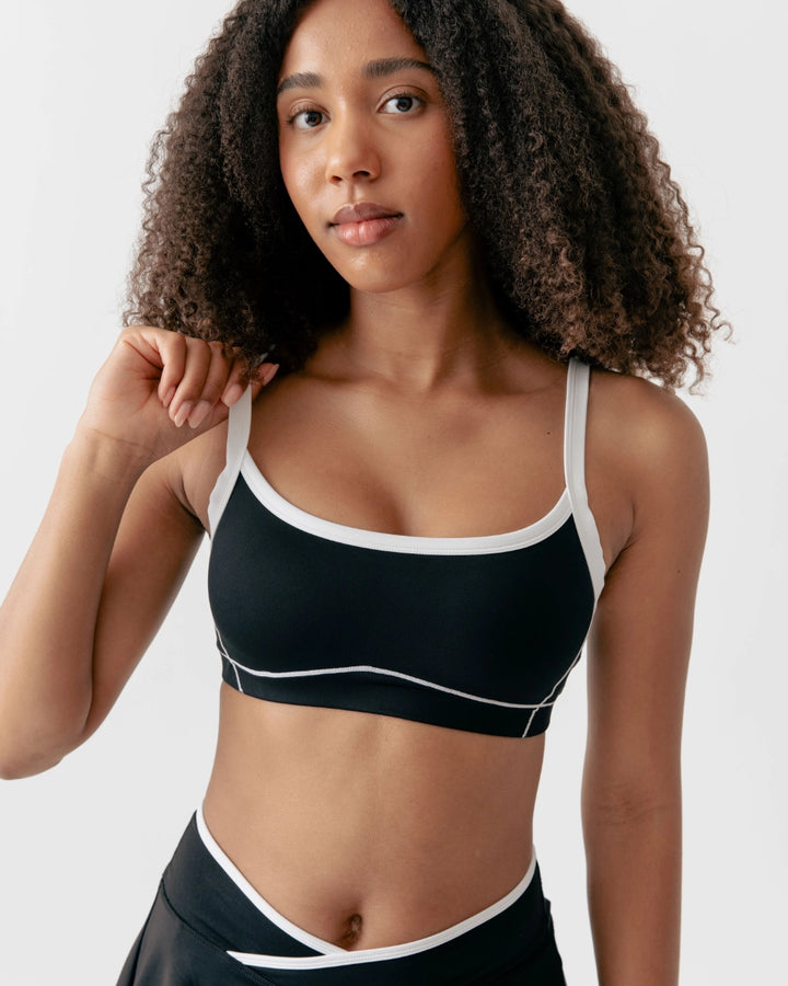 Woman wearing a black sports bra with white straps on a plain background