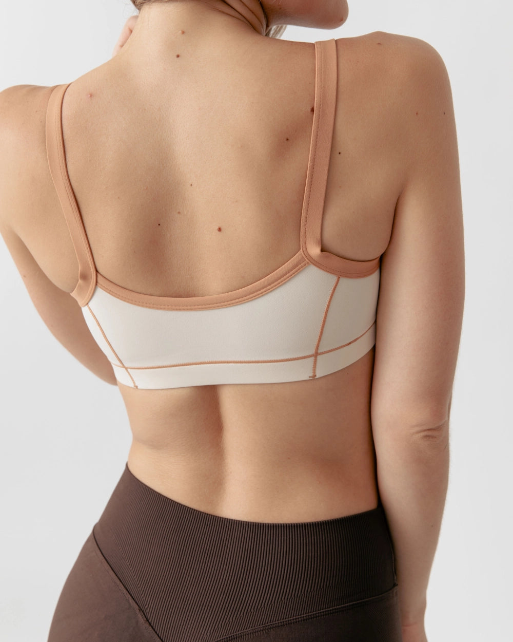 Person wearing a beige sports bra and brown leggings on a light gray background
