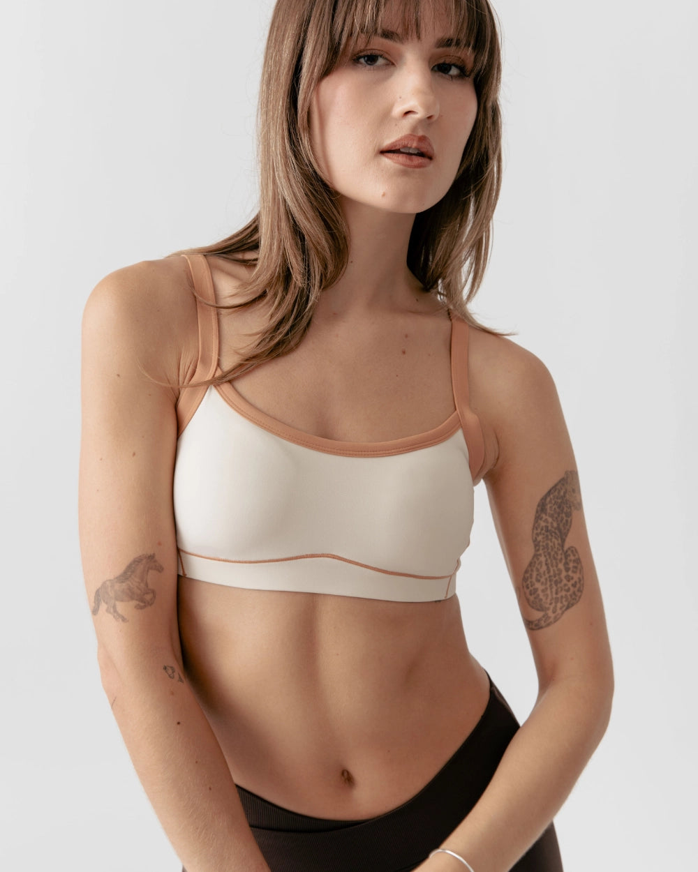 Woman wearing a beige sports bra and black leggings on a plain background