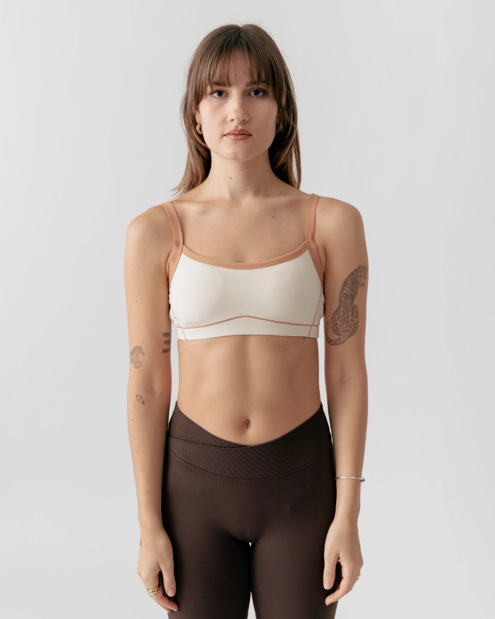 Woman wearing a beige sports bra and brown leggings on a plain background