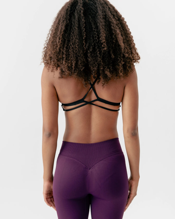 Person wearing a purple athletic outfit with a black strappy top on a white background