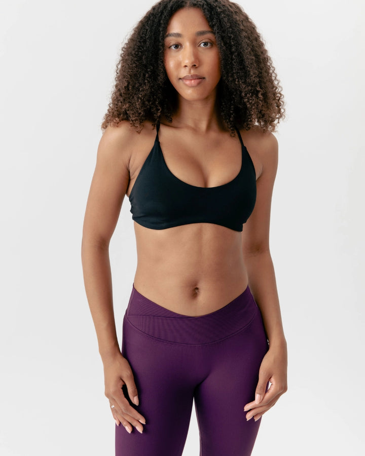 Woman wearing a black sports bra and purple leggings on a white background