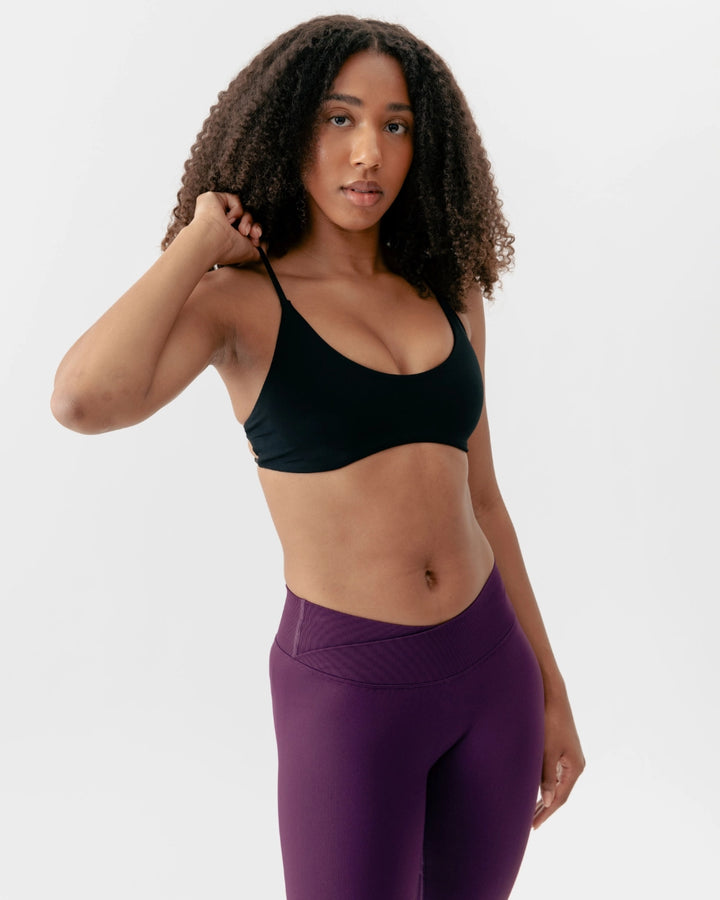 Woman wearing a black sports bra and purple leggings on a white background