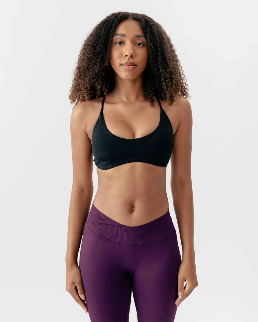 Woman wearing a black sports bra and purple leggings on a white background