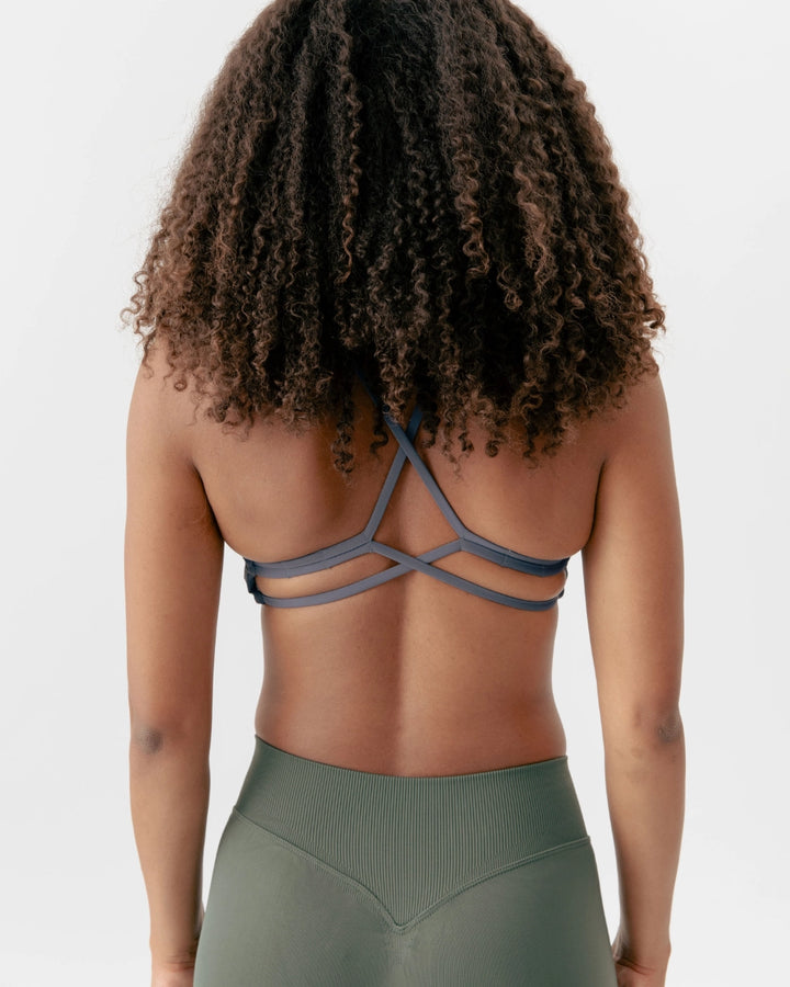 Person wearing a gray strappy top and green leggings on a plain background