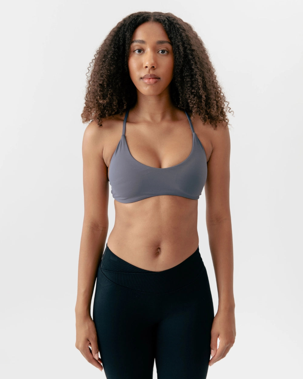 Woman wearing a gray sports bra and black leggings on a white background