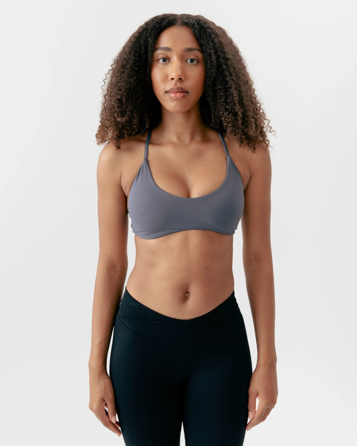 Woman wearing a gray sports bra and black leggings on a white background