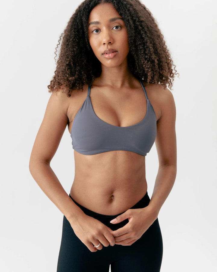Woman wearing a gray sports bra and black leggings on a white background