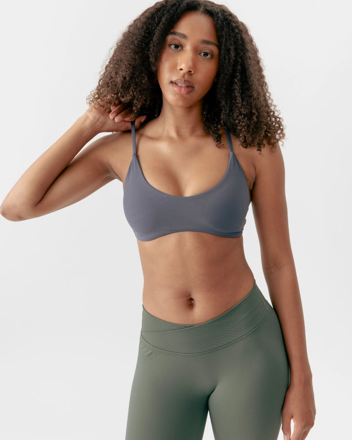Woman wearing a gray sports bra and green leggings on a white background