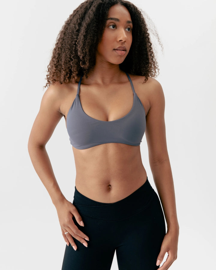 Woman wearing a gray sports bra and black leggings on a white background