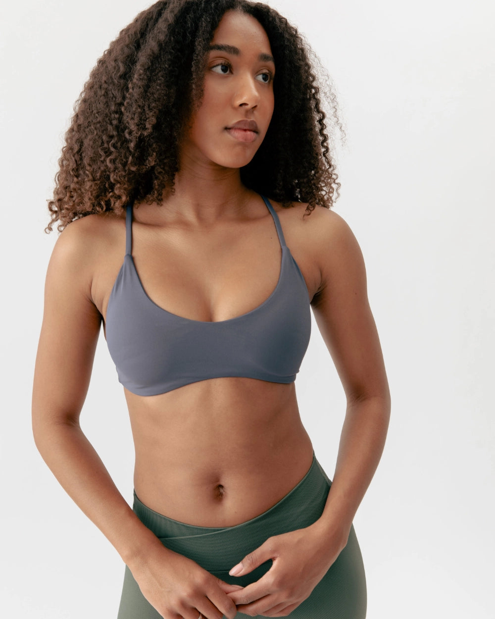 Woman wearing a gray sports bra and green leggings on a white background