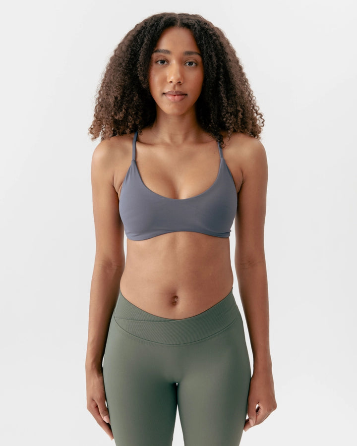 Woman wearing a gray sports bra and green leggings on a white background