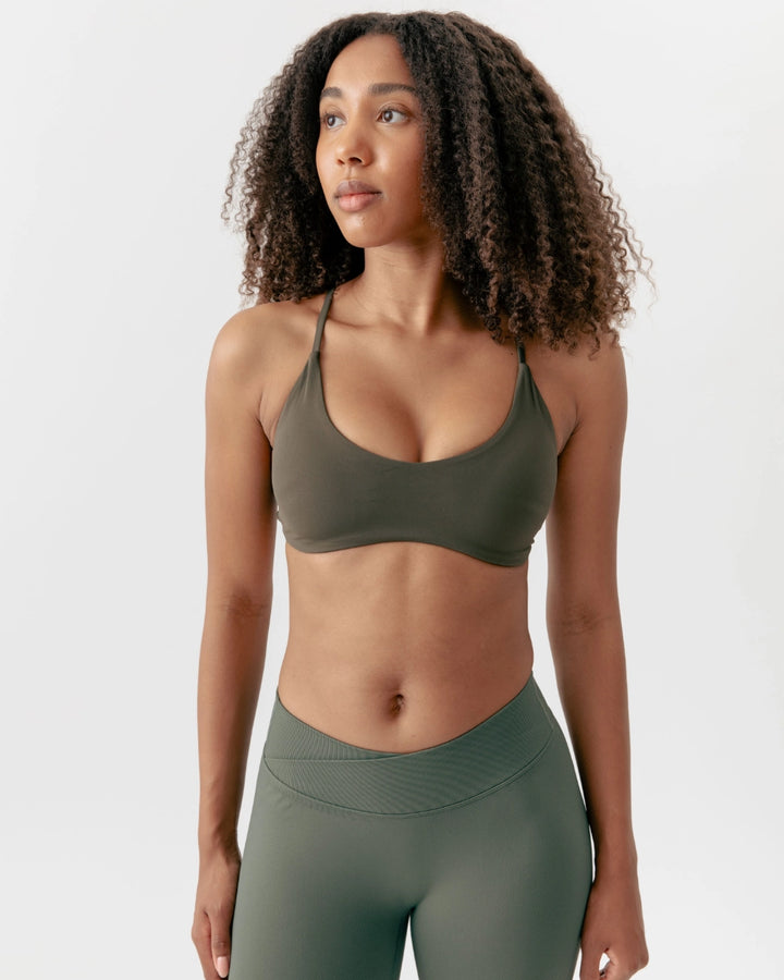 Woman wearing a green sports bra and leggings on a white background
