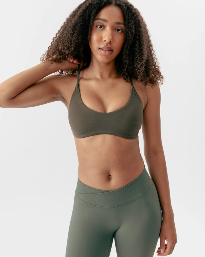 Woman wearing an olive green sports bra and leggings on a white background